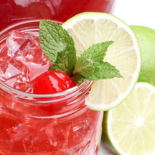 a glass of cherry limeade with limes around it